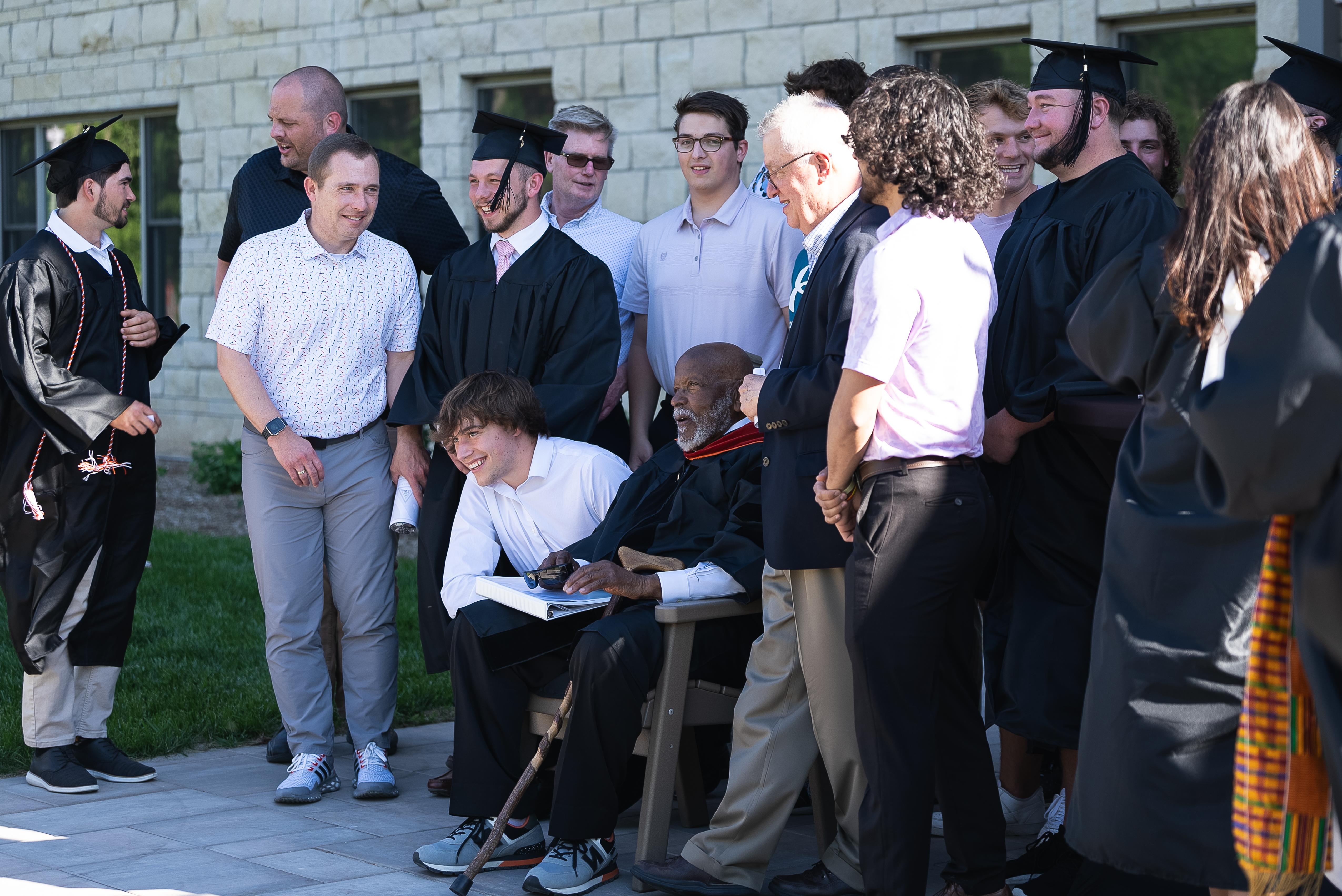 A group of men gather together for a photo. One of them is sitting, one kneeling, while the others stand behind. 